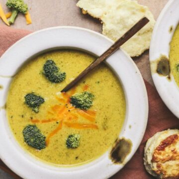 Two bowls of broccoli cheddar soup on a napkin with spoons.