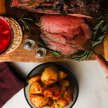 Medium rare prime rib on a cutting board, someone grabbing slice with fork.