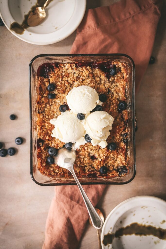 Apple and blueberry crumble in a baking sheet, with three scoops of ice cream. 