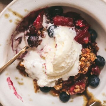 A bowl of apple and blueberry crumble with ice cream.