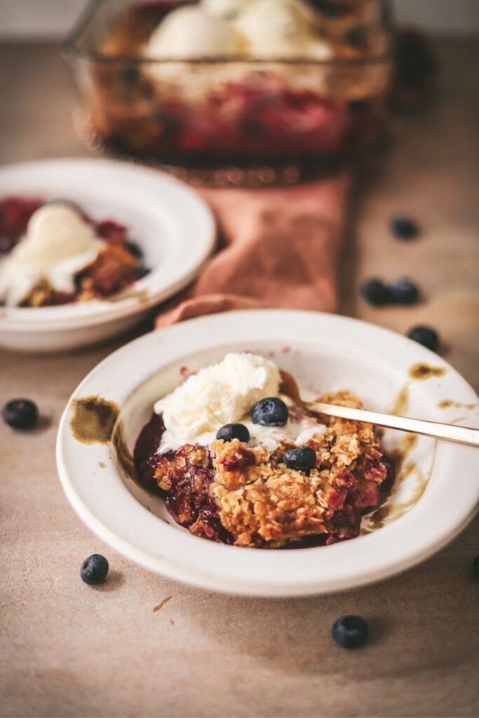 A bowl of apple and blueberry crumble with ice cream. 