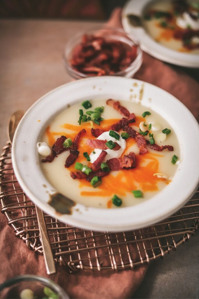 A bowl of potato soup with napkin, trivet and garnishes. 