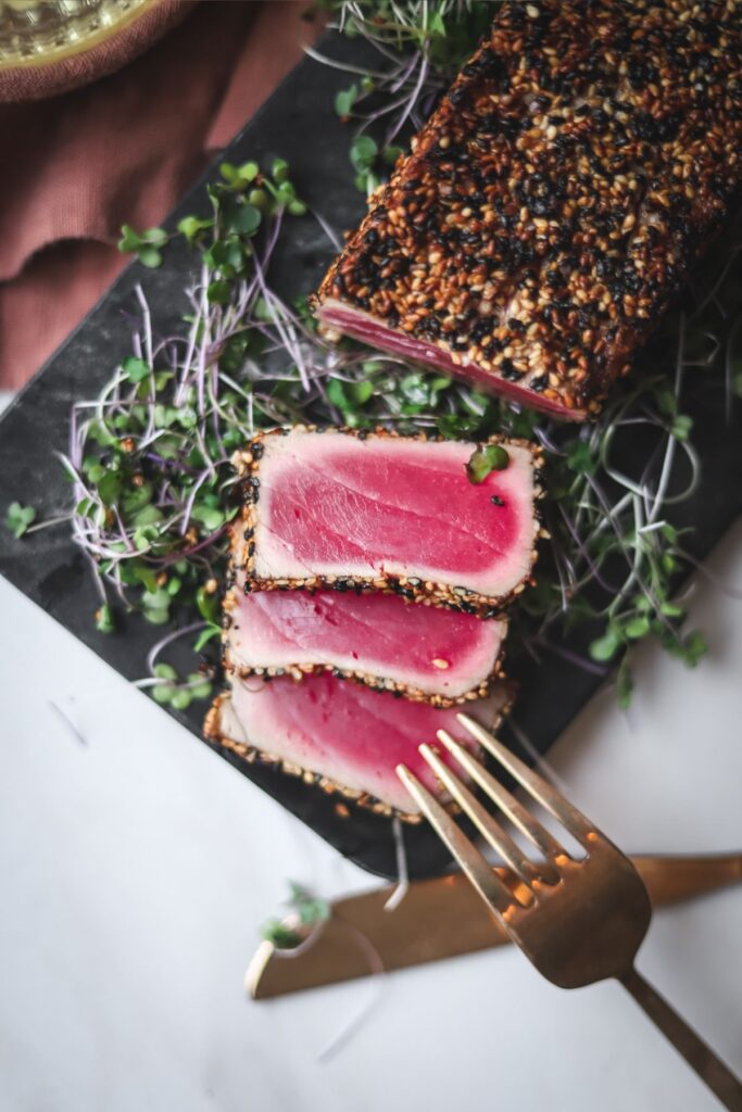 Seared ahi tuna with sesame seeds, and a gold fork and knife.