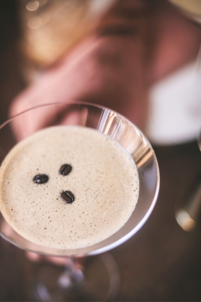 An espresso martini with foam and three coffee beans floating on top. 
