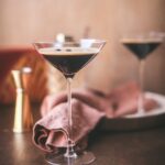 Two espresso martinis with a thin layer of foam and coffee beans on top.