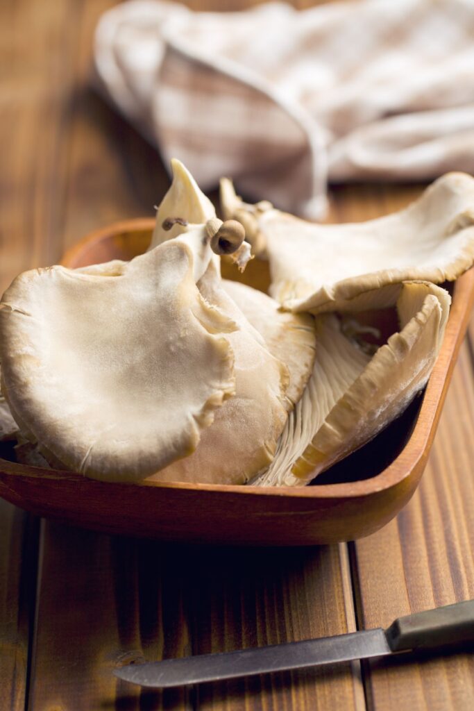 Several oyster mushrooms, stems removed in a small bowl on a wooden table. 
