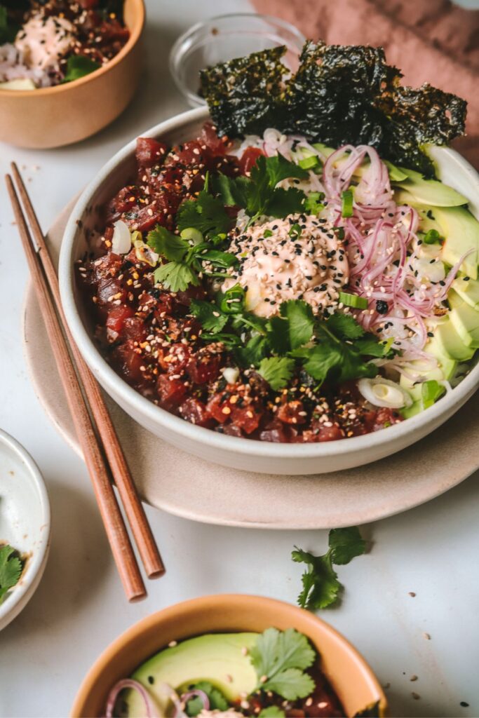 A Poké bowl on a plate, served with avocado and cilantro, with spicy mayo. 