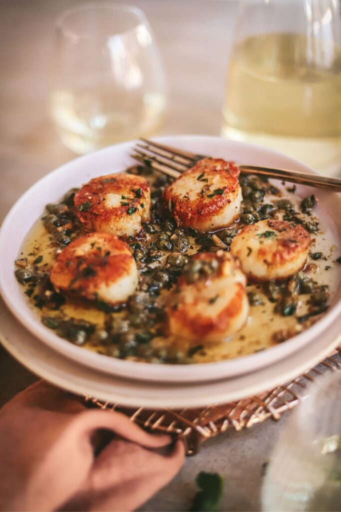 A plateful of scallops with capers and lemon. 