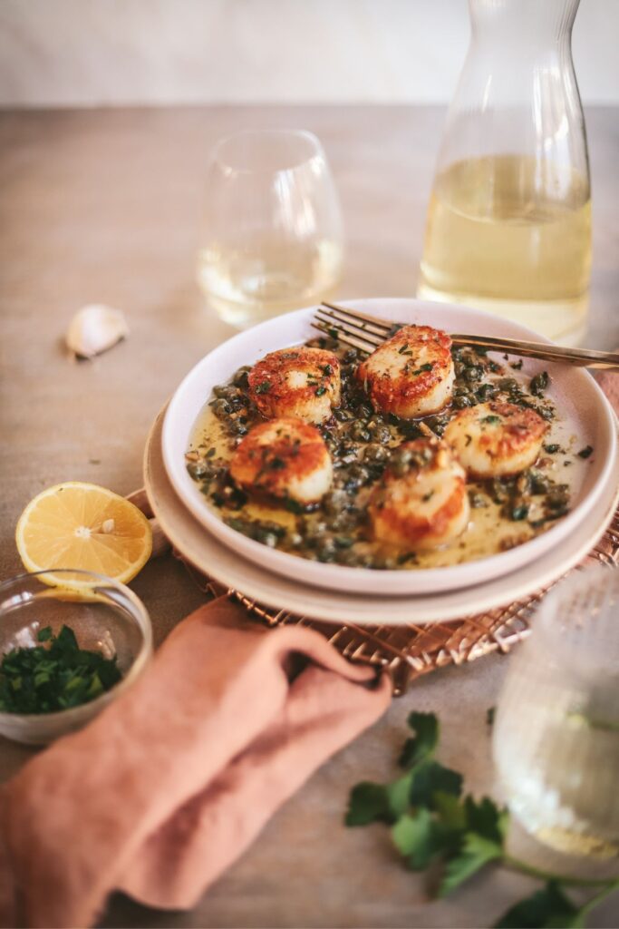Seared scallops with lemon, parsley, and white wine on a plate. 