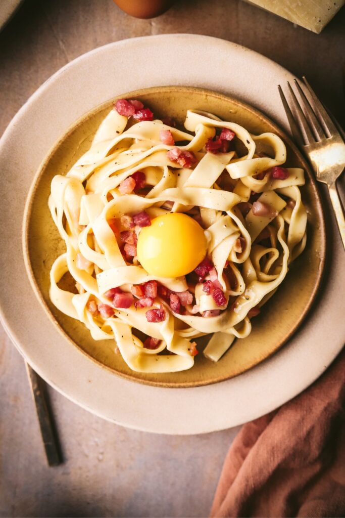 A plate of tagliatelle carbonara with and egg yolk on top. 