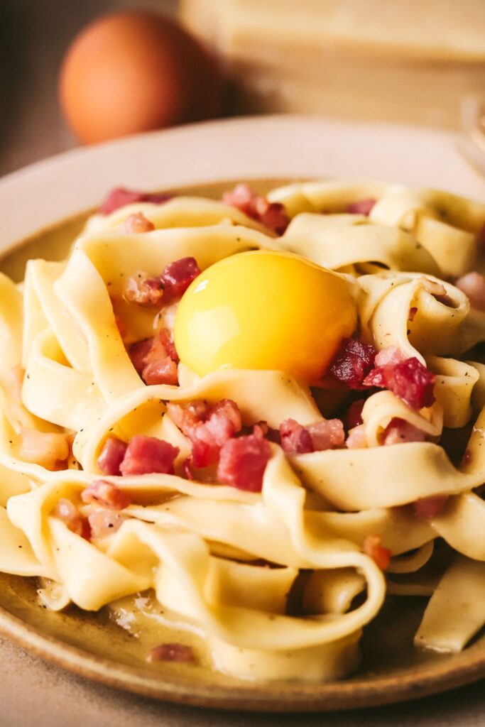 Tagliatelle carbonara with parmesan cheese and eggs in the background. 