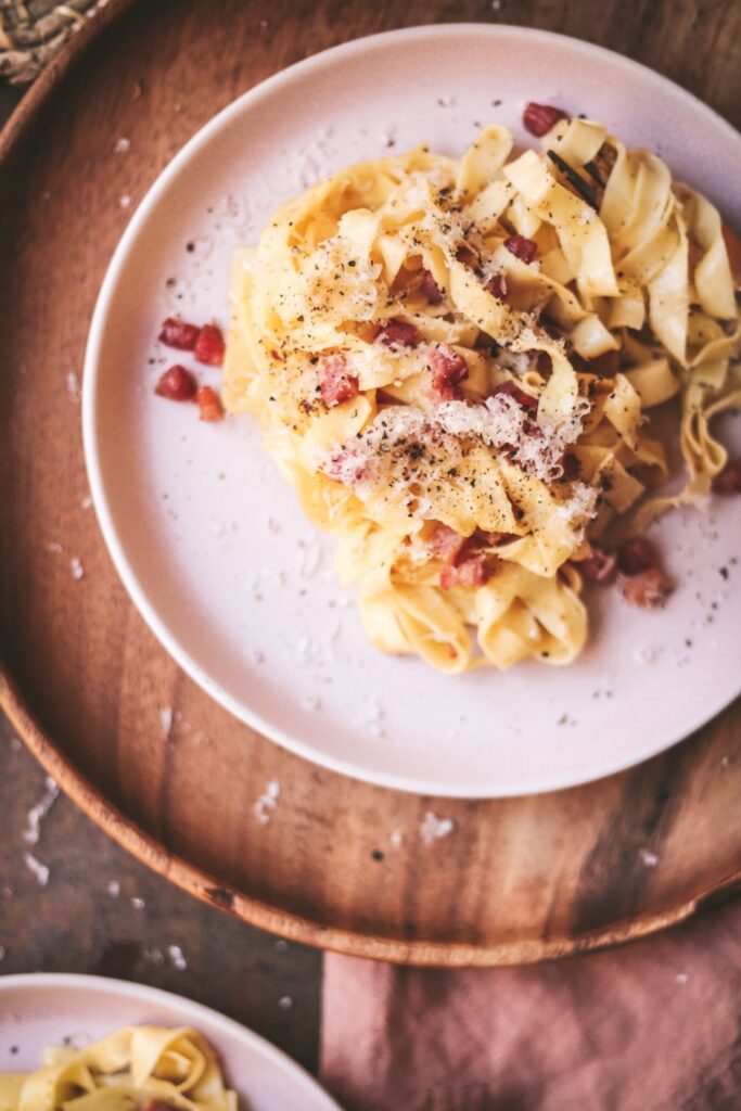 A plate of tagliatelle carbonara, with a napkin and wooden placemat. 