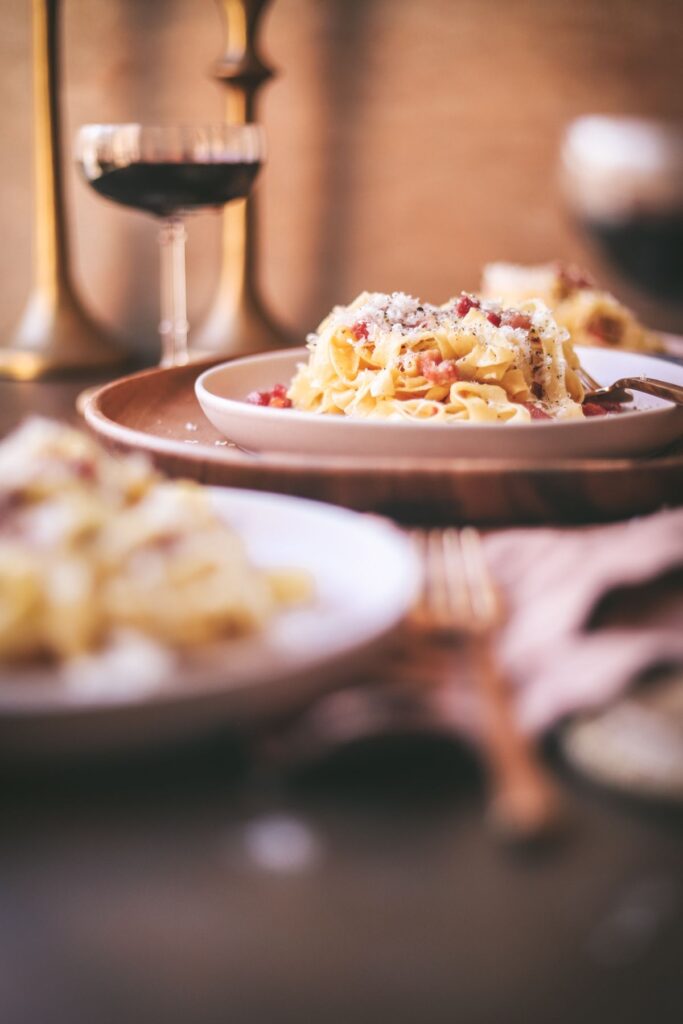 A straight on side shot of a plateful of carbonara with red wine.
