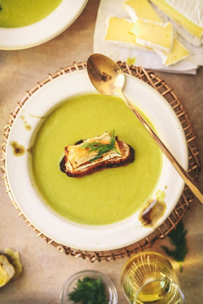 Asparagus soup with a gold spoon and brie on the side. 