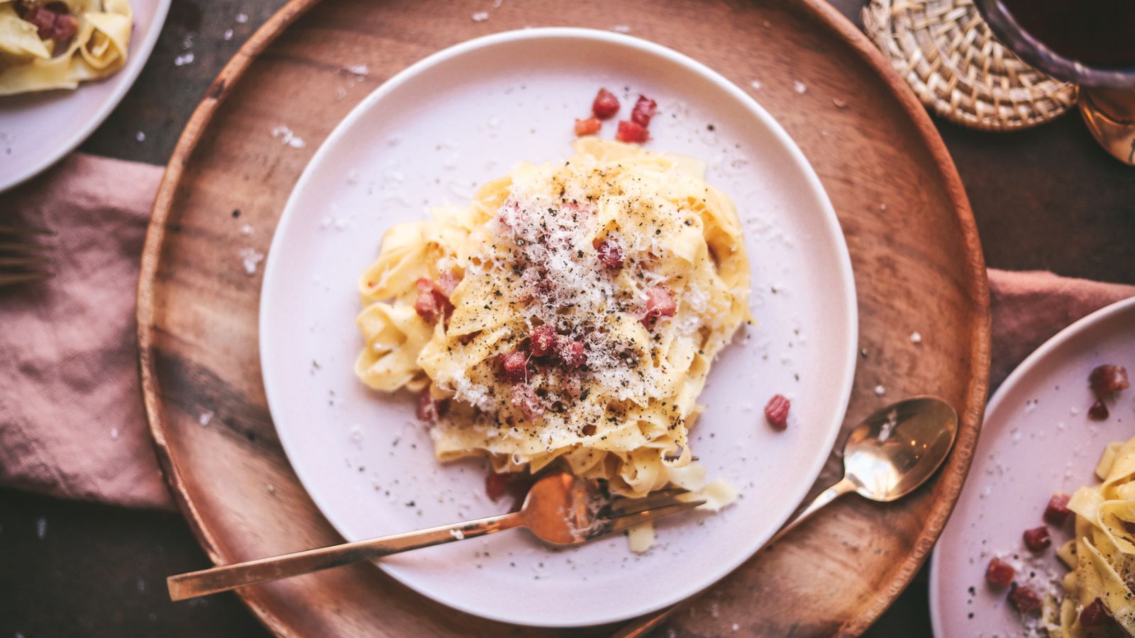 Tagliatelle carbonara with a wooden placemat and gold fork. 