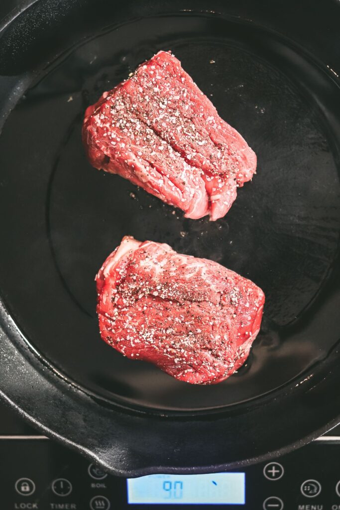 Placing the steaks in a smoking hot cast-iron skillet to sear. 