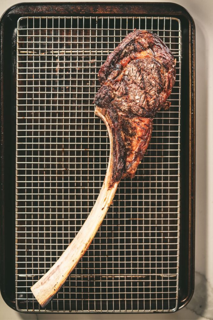 Tomahawk steak on a cooling rack inside a baking sheet. 