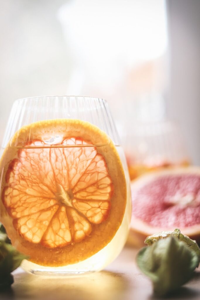 White sangria in front of a window with light coming through the grapefruit slice. 