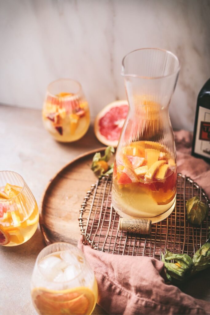 A tall clear pitcher of white sangria with fresh fruit. 
