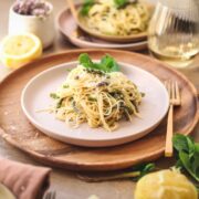 A pile of asparagus pasta with lemon and mint on a wooden placemat.