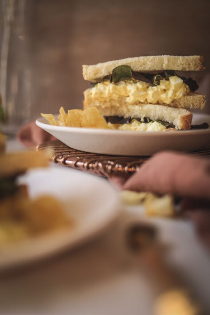 An egg salad sandwich with lettuce and chips on a plate. 