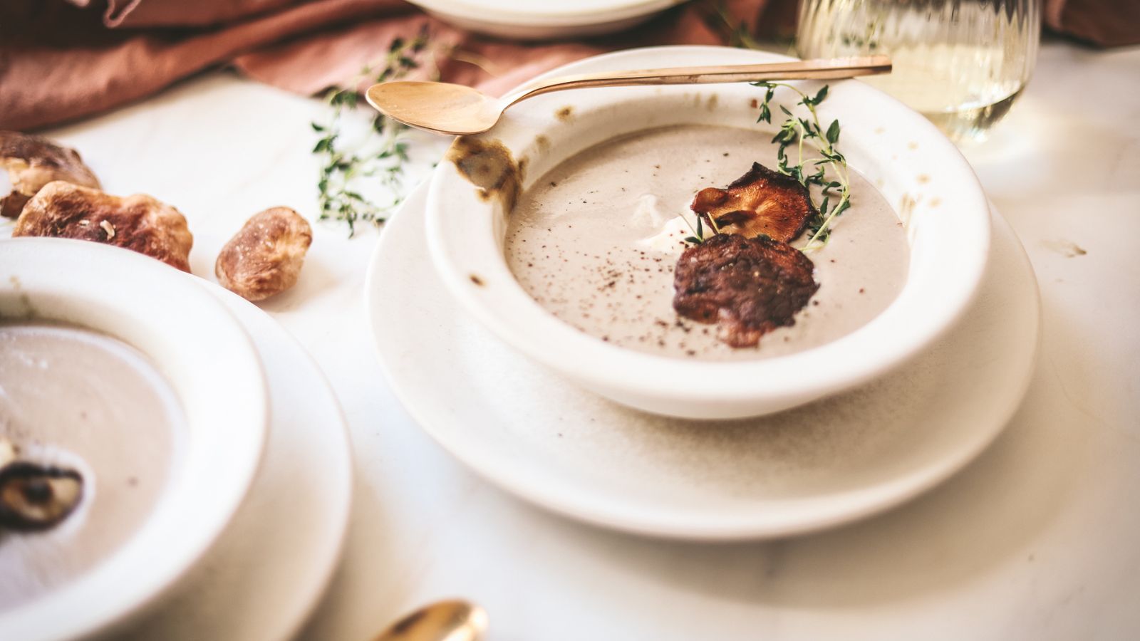 A bowl of cream of mushroom soup with seared shiitakes on top, and gold cutlery. 