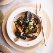 A bowl of mussels in white wine sauce with gold cutlery.