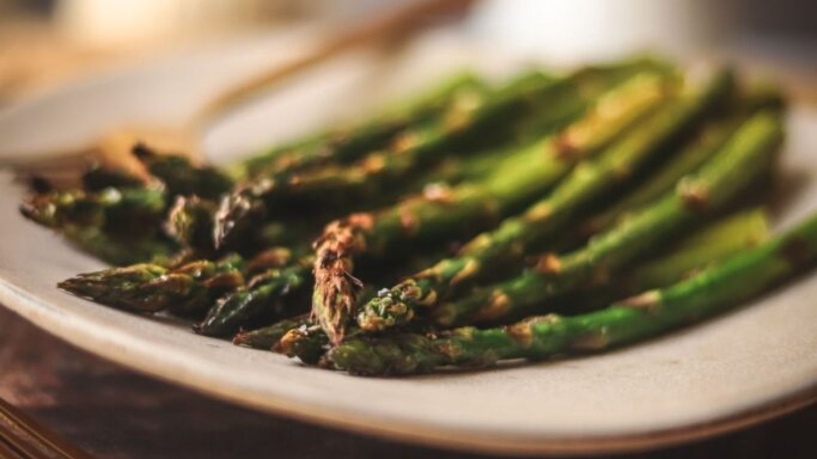 A plate of broiled asparagus on a wooden cutting board. 
