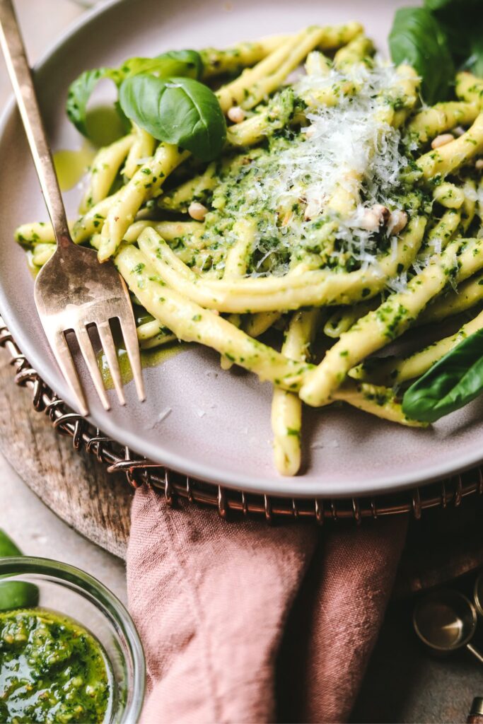A close up of the pasta al pesto with a gold fork and fresh basil.