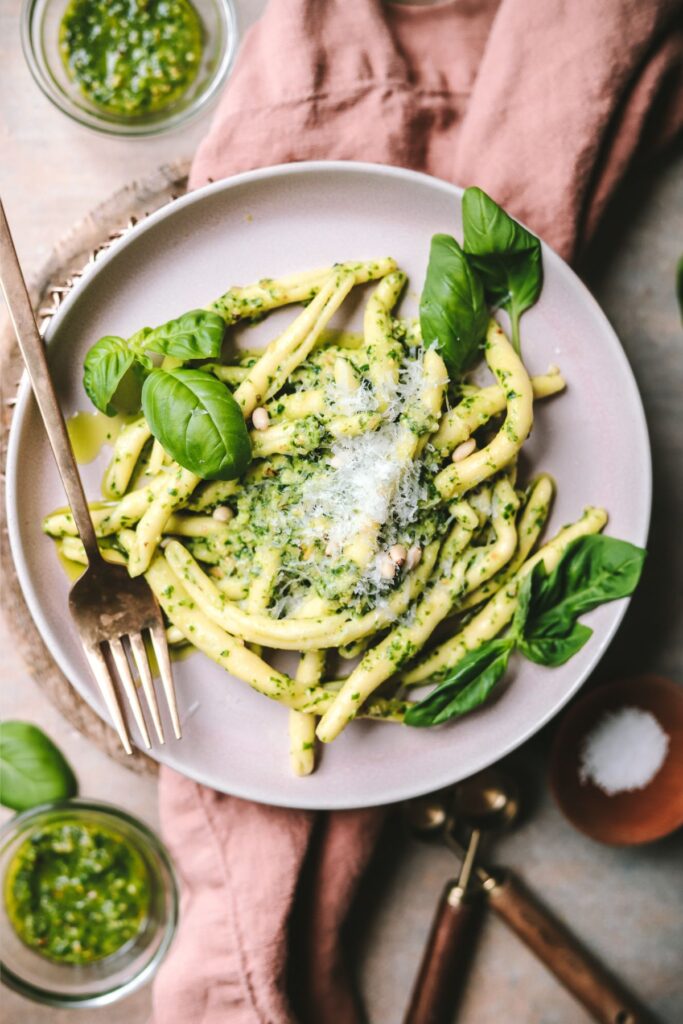A plate of pasta al pesto with fresh basil and parmesan cheese. 