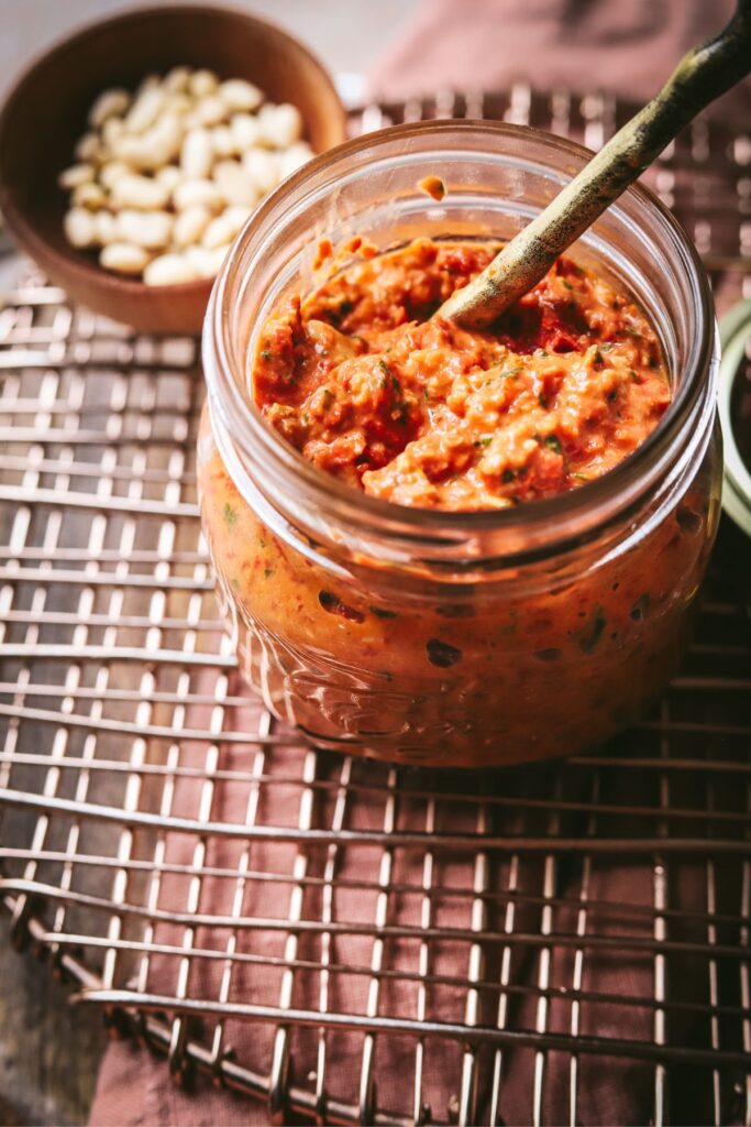  A jar of pesto rosso with some pine nuts and a spoon. 