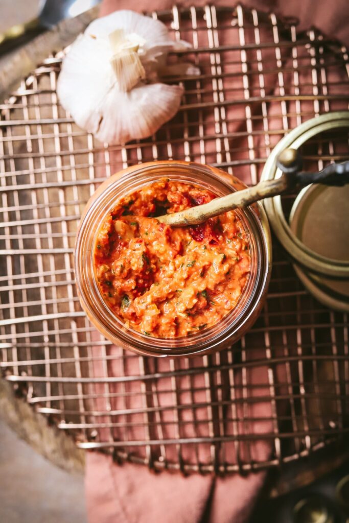 A jar of red pesto, with garlic and a spoon. 