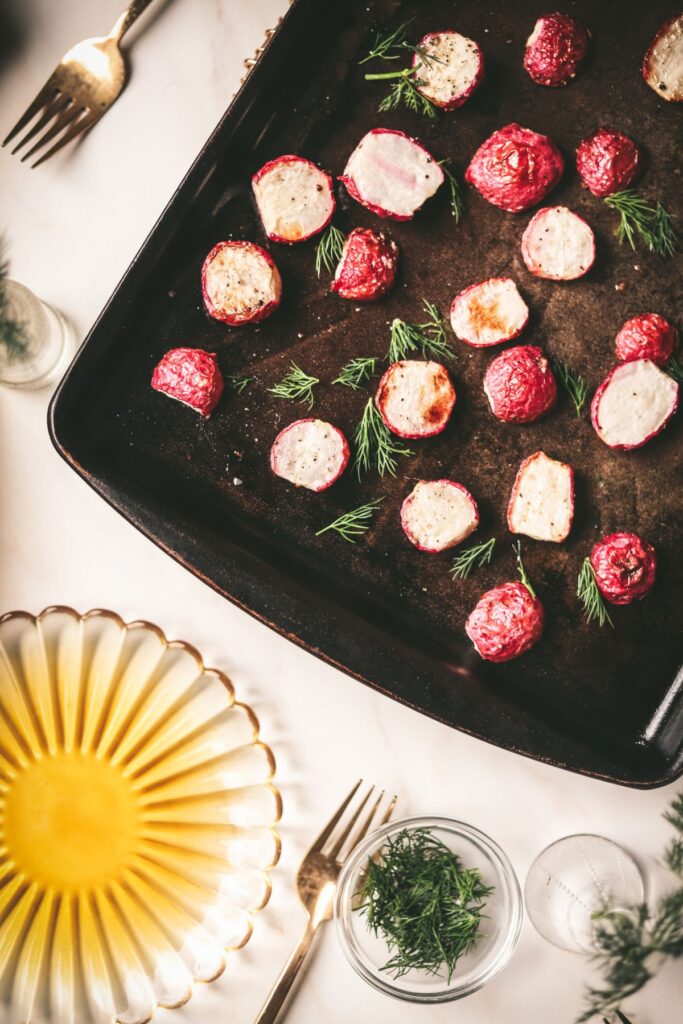 Roasted radishes on a baking sheet with yellow plate and dill. 
