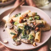 A plate of vegetable pasta with mushrooms broccoli and hazelnuts.