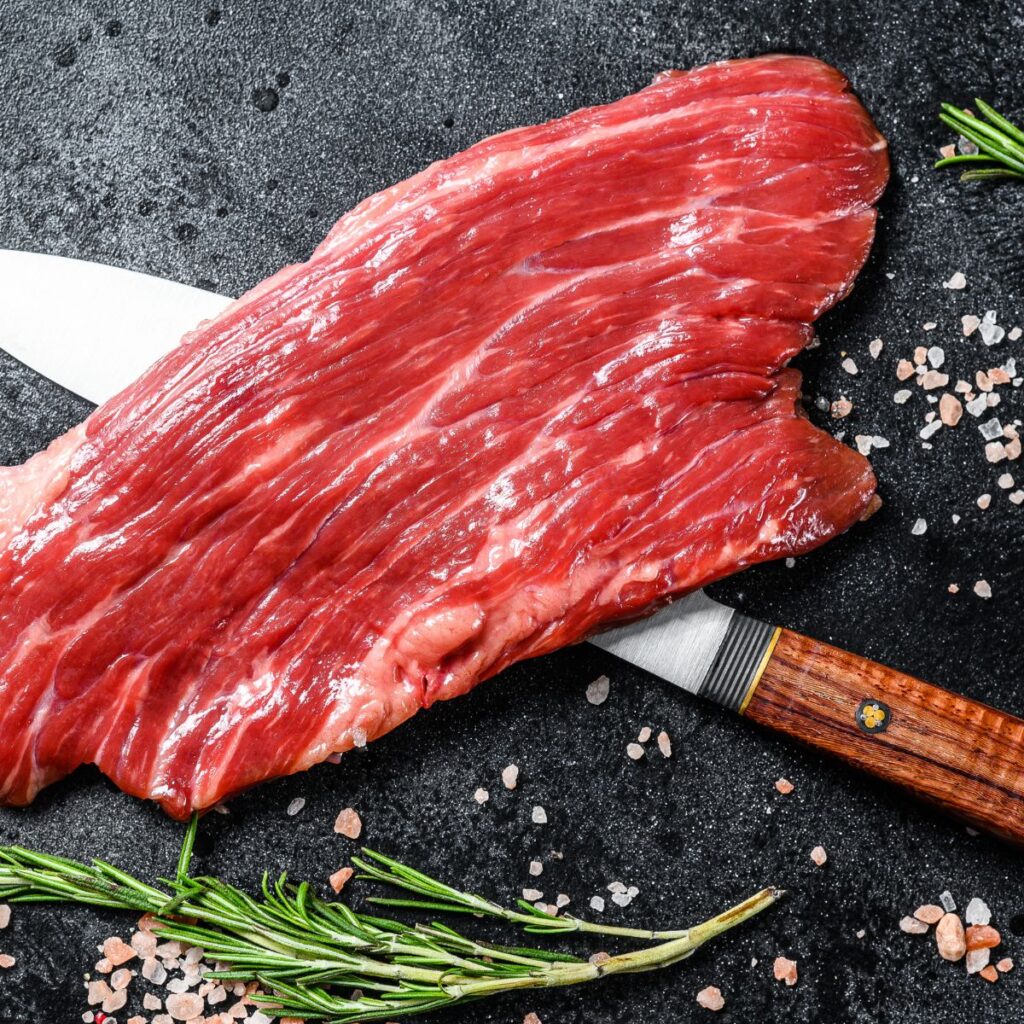 A photo of a raw flank steak over a knife.