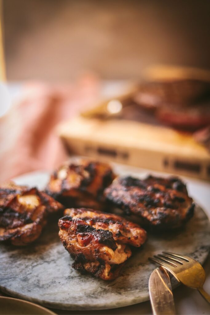 Four grilled chicken thighs on a stone serving platter. 
