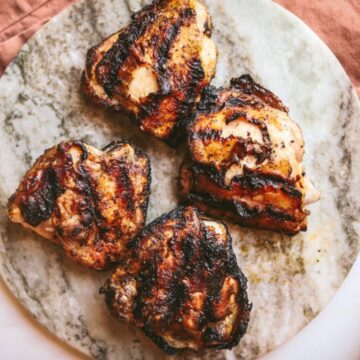 Grilled chicken thighs on a marble serving board.