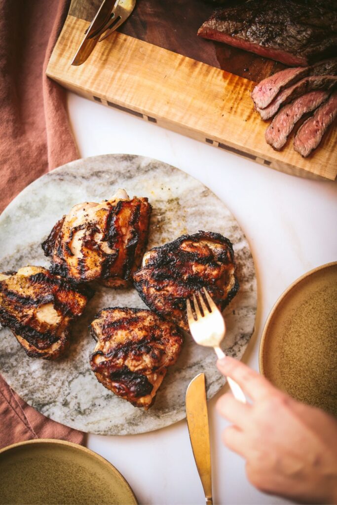 Grilled chicken thighs with someone grabbing one off the plate with a fork. 