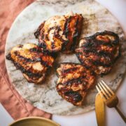 Four grilled chicken thighs on a stone plate.