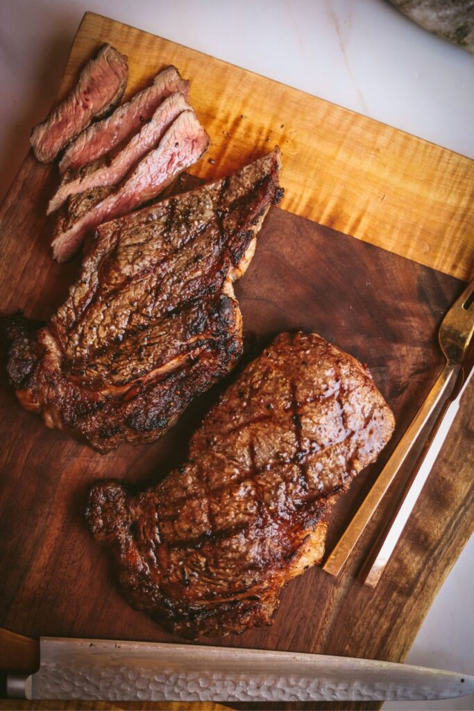 Two grilled ribeye steaks on a wooden cutting board. 