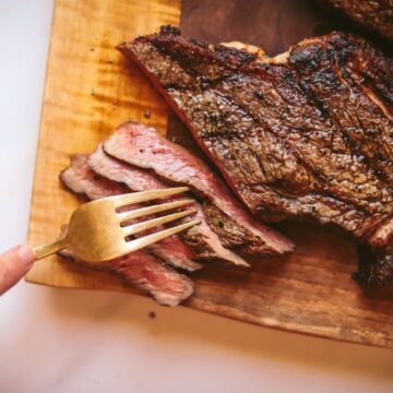 Ribeye steak on a cutting board with someone taking a forkful.