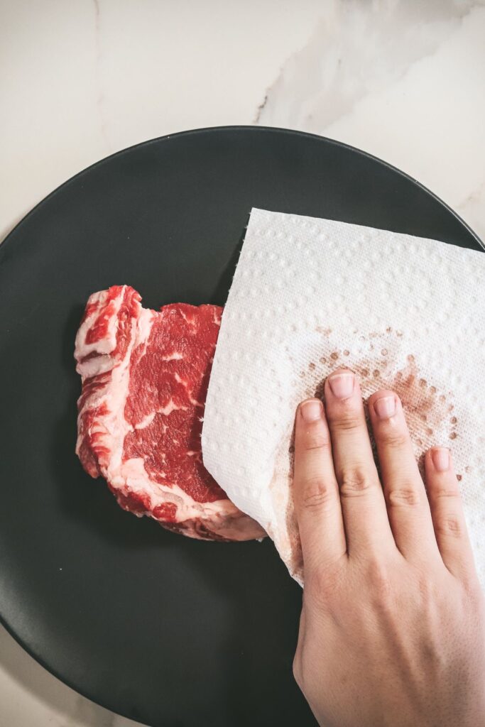 Patting the ribeye dry with paper towel.