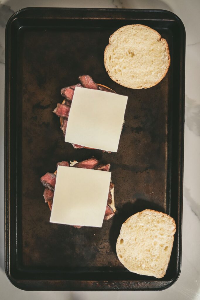 cheese on the steak, bun tops added to baking sheet. 