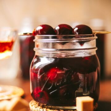 A jar of bourbon soaked cherries and cherries on a cocktail pick.
