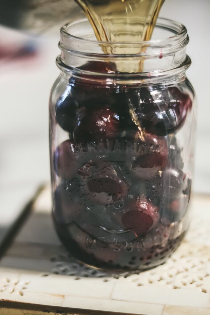 Pouring bourbon mixture into the mason jar with the cherries. 
