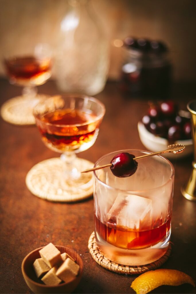 A smoked old fashioned with sugar cubes and cherries in the background.