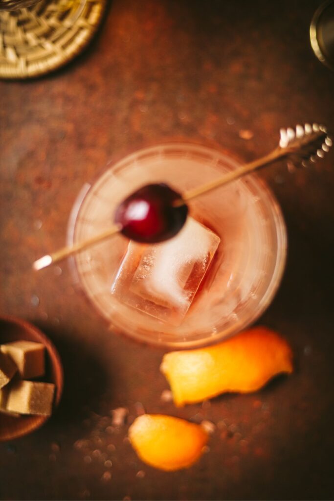 A smoking old fashioned garnished with a cocktail cherry.