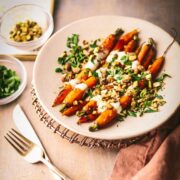 A plate of honey roasted carrots, garnished with parsley, orange crème fraiche and pistachios.