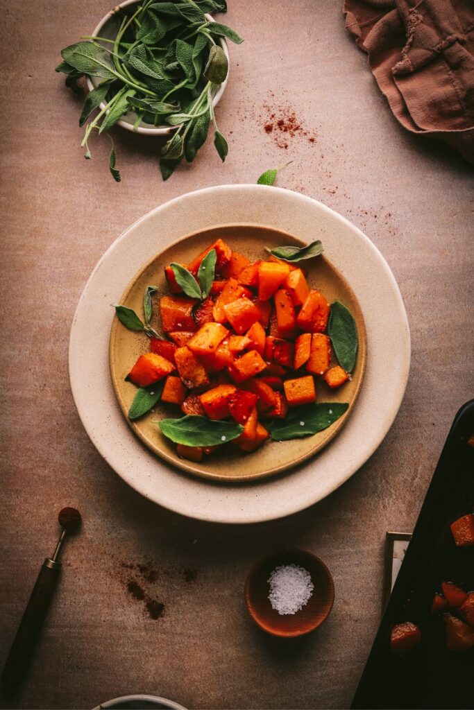 Roasted butternut squash on a plate with spices and sage leaves. 