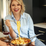 Cara Campbell, eating homemade fresh pasta straight from the pan, smiling at the camera.